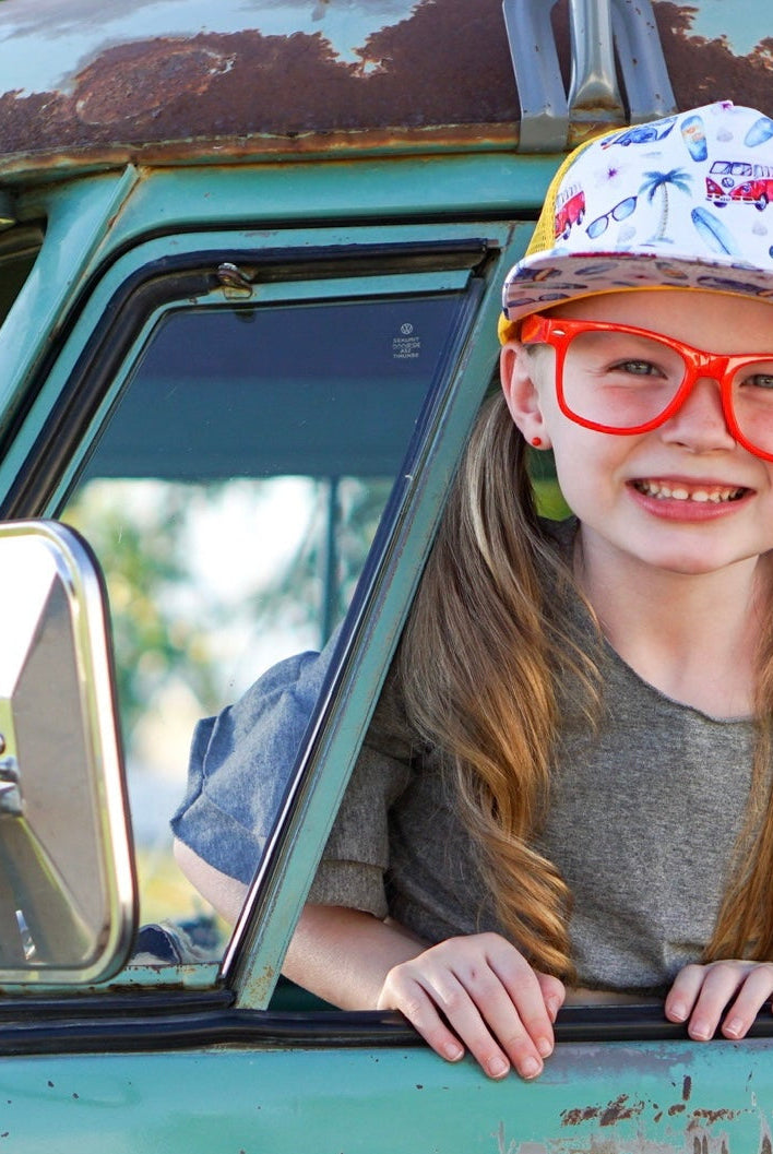 Young girl with red glasses and a cap leaning out of a vintage green truck window.