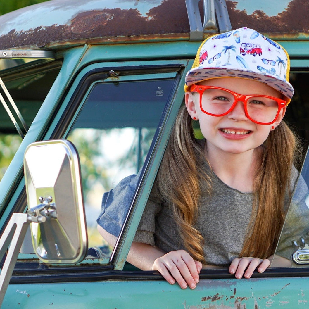Young girl with red glasses and a cap leaning out of a vintage green truck window.